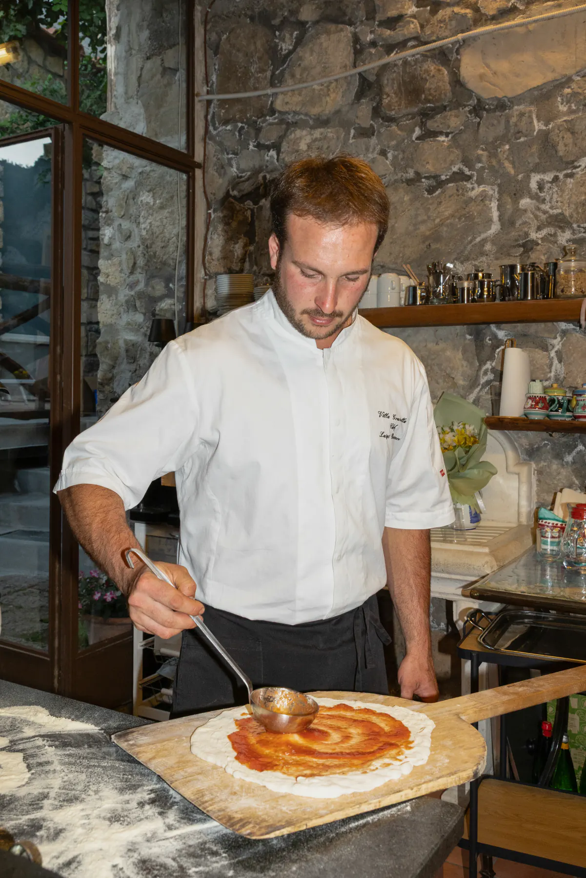 Lo chef Luigi stende la salsa sulla pizza, davanti al forno a legna della villa