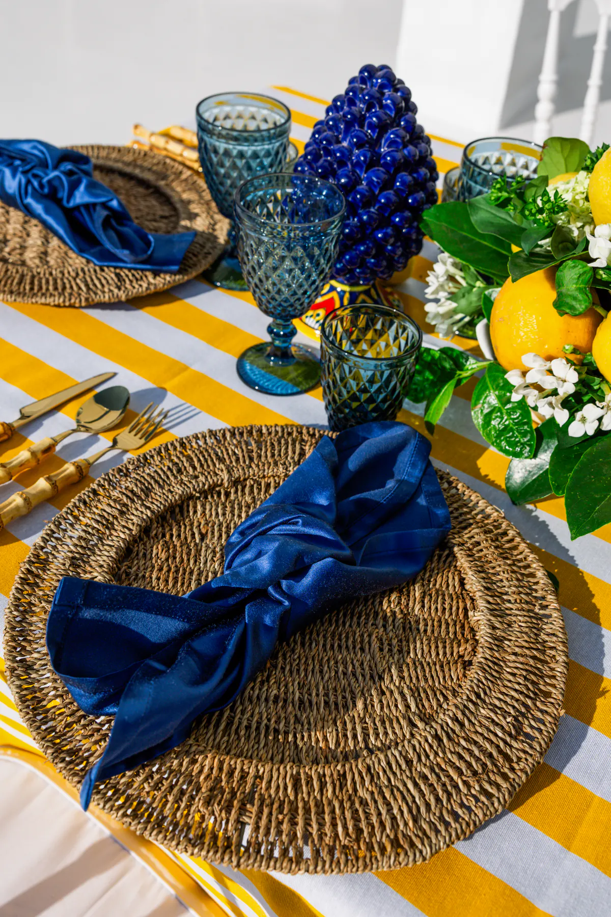 Il dettaglio del coperto: piatto di rattan, tovagliolo blu e pigna di ceramica