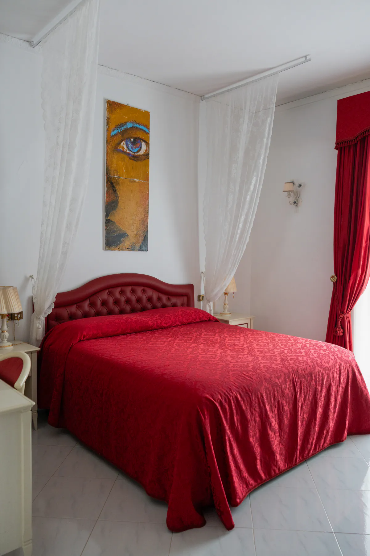 La camera rossa di Villa Graziella, con la testata capitonné e il velo bianco sul letto