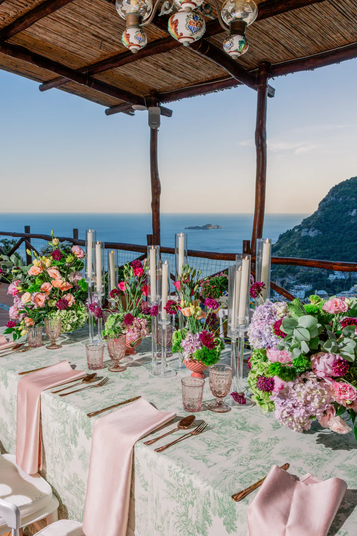 La tavola del ricevimento apparecchiata sotto il pergolato, con fiori e candele e il mare davanti